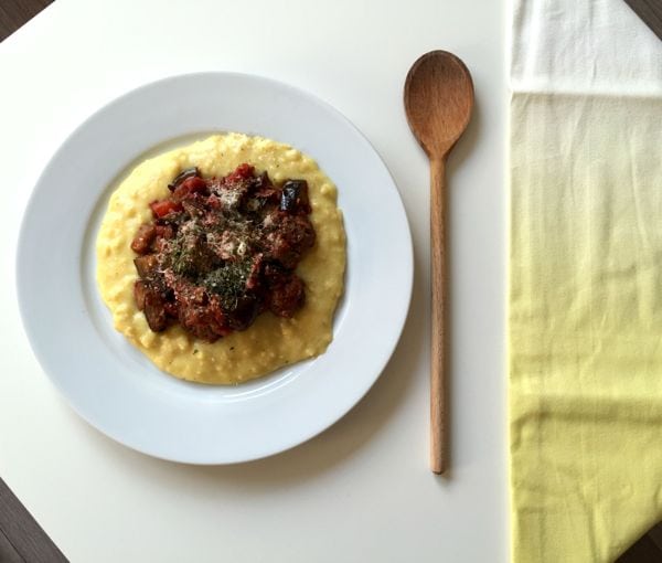 Low FODMAP polenta on a plate with a yellow napkin and wooden spoon next to it
