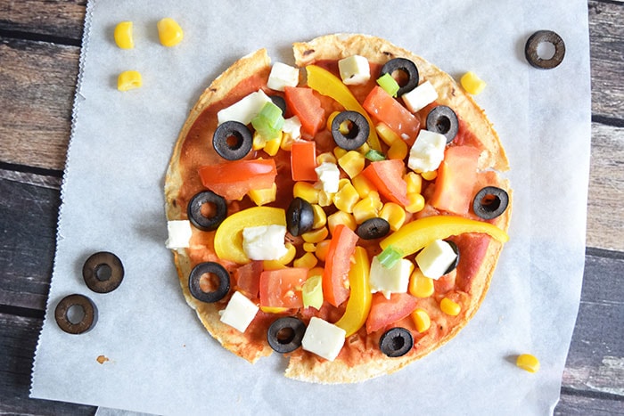 A low FODMAP tortilla pizza with corn and olives next to it, photographed from above