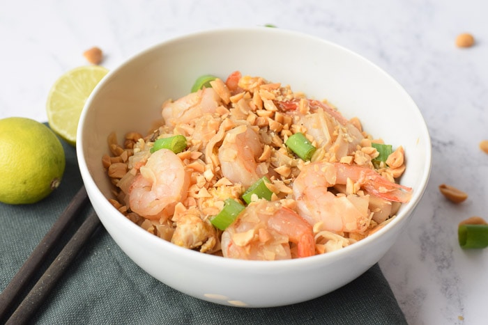 Low FODMAP pad thai in a bowl with shrimps with limes next to it