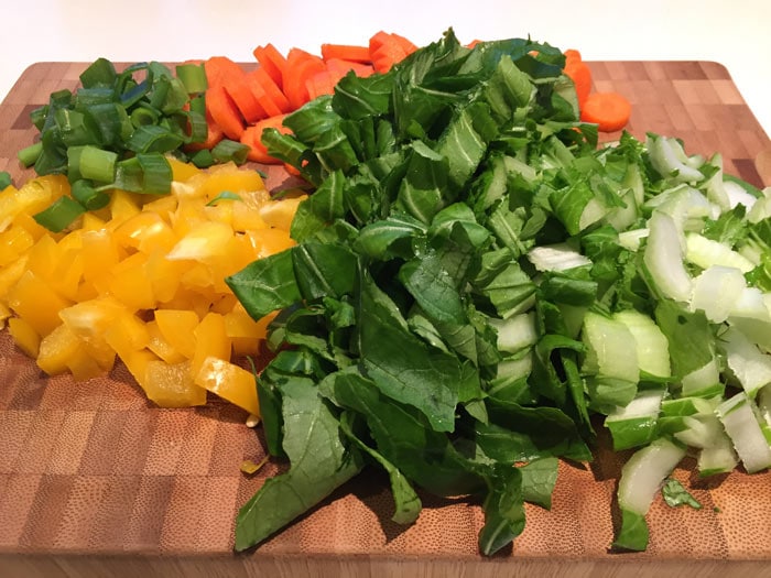 A wooden cutting bord with bell pepper, carrot and bok choy on it