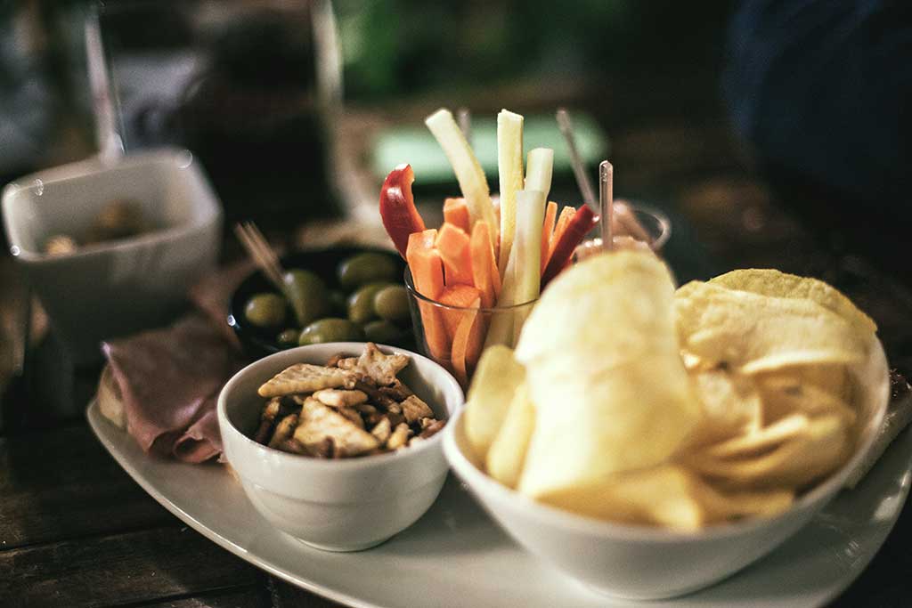 A platter with snacks: chips, olives, crackers and veggies