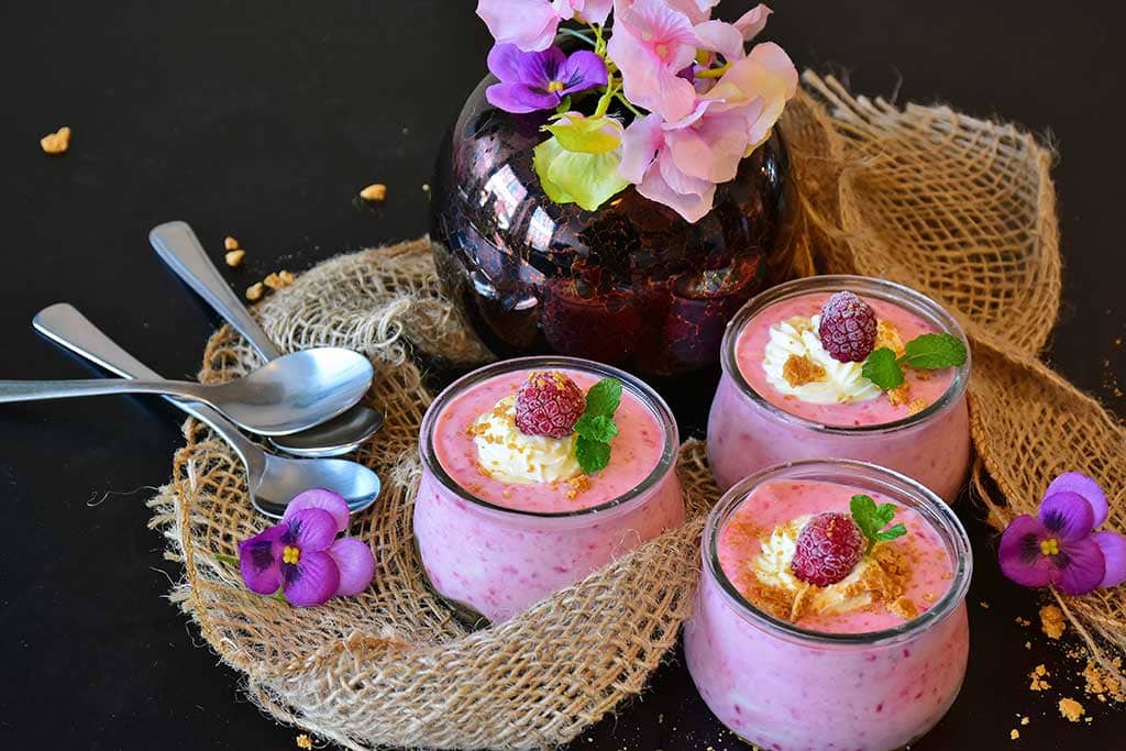 Three bowls with pink yoghurt with flowers next to it