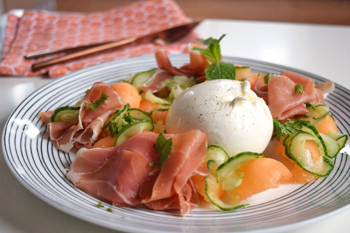 Melon salad with parma ham and burrata on a plate with stripes