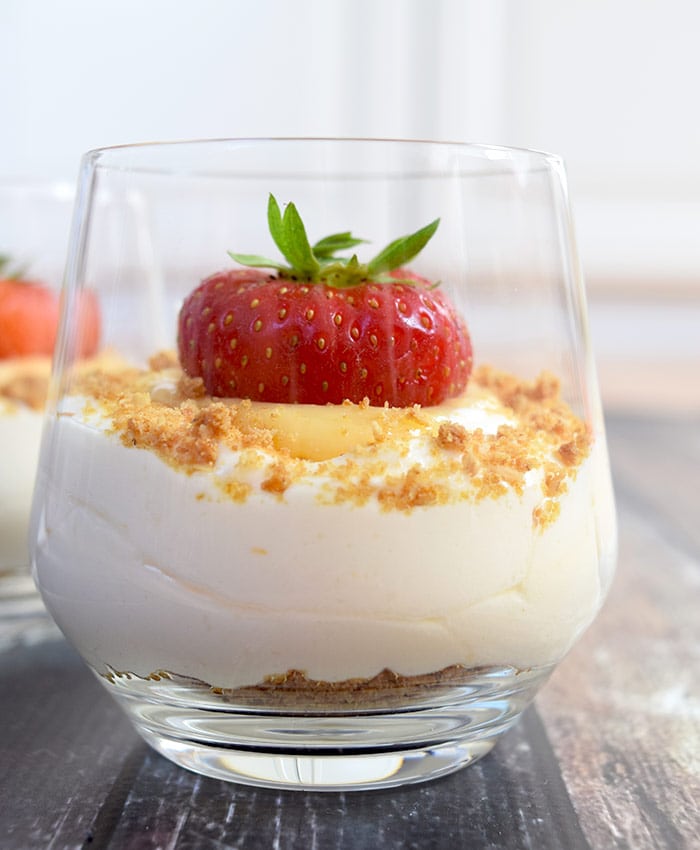 A glass of low FODMAP lemon mousse with lemon curd and a strawberry photographed from the side
