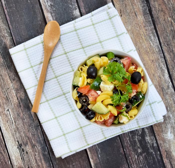 A bowl with low FODMAP greek pasta salad with a spoon next to it
