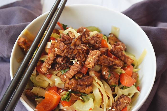 Rice noodles with crunchy sesame tempeh in a bowl with chopsticks on top