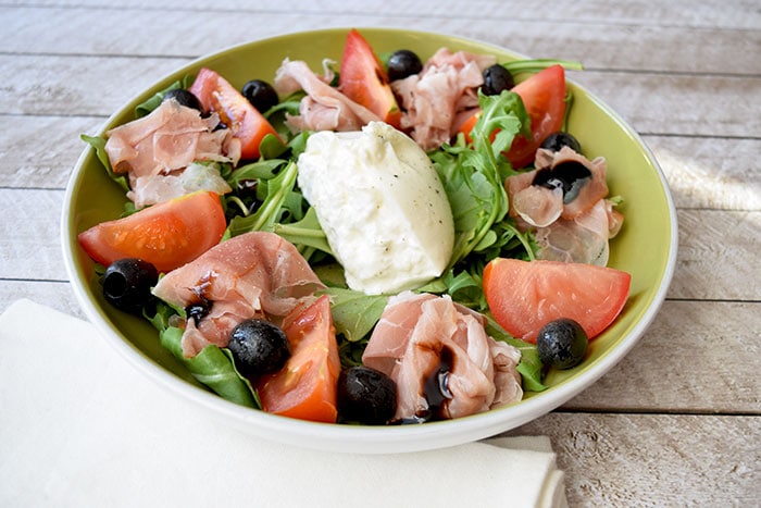 A bowl with a burrata salad with tomato and parma ham