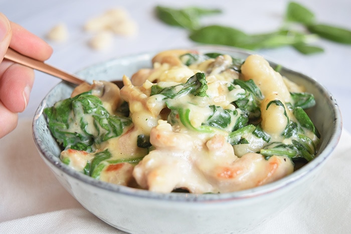 A hand sticking a spoon in a bowl of low FODMAP creamy gnocchi