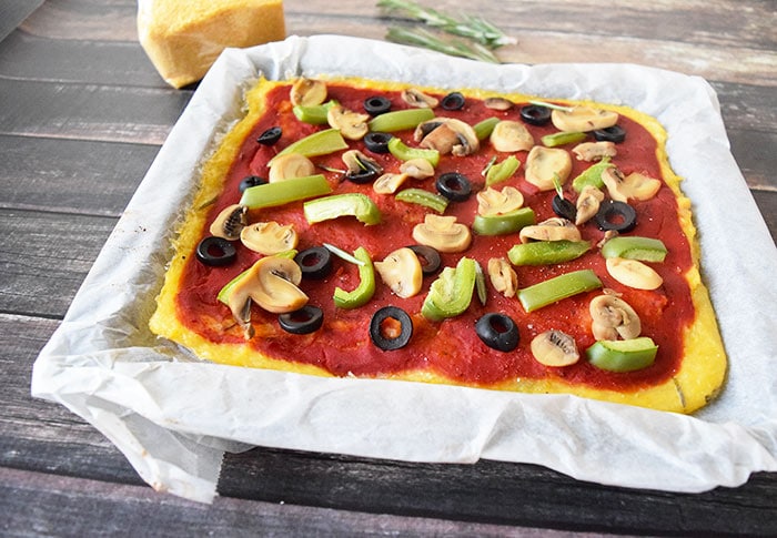 Een low FODMAP vegan polenta pizza met groene paprika, champignons en olijven