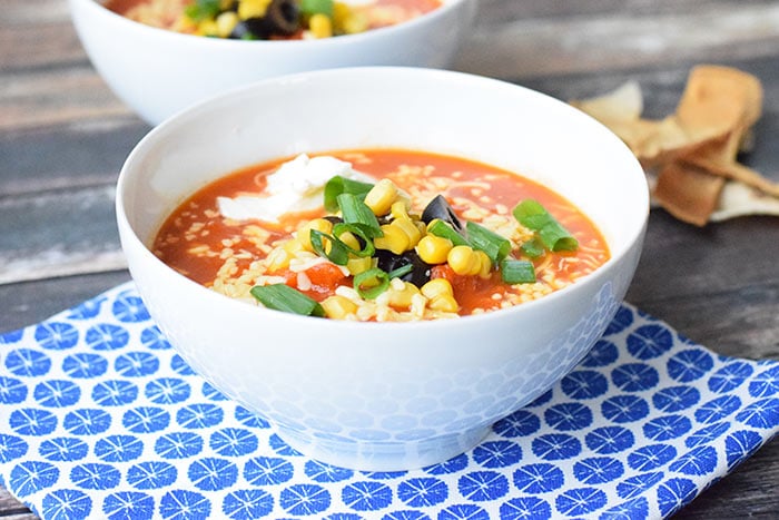 A bowl of low FODMAP tortilla soup topped with creme fraich, corn and olives
