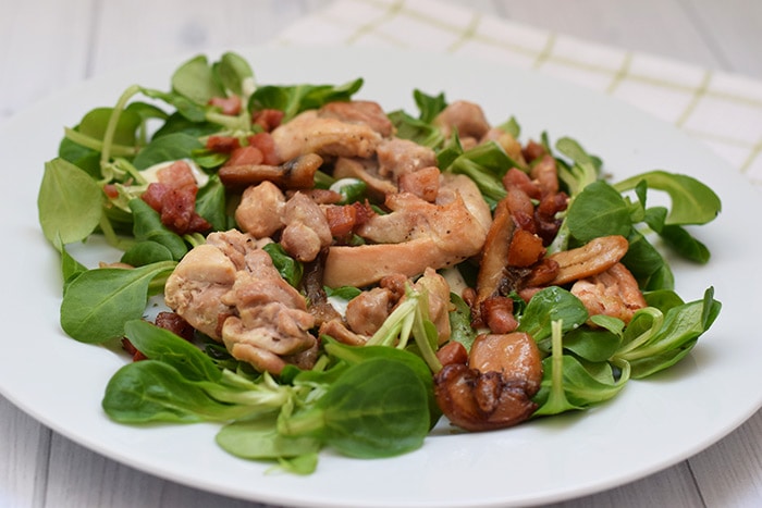 A lukewarm salad with chicken thigh, mushrooms and bacon on a plate