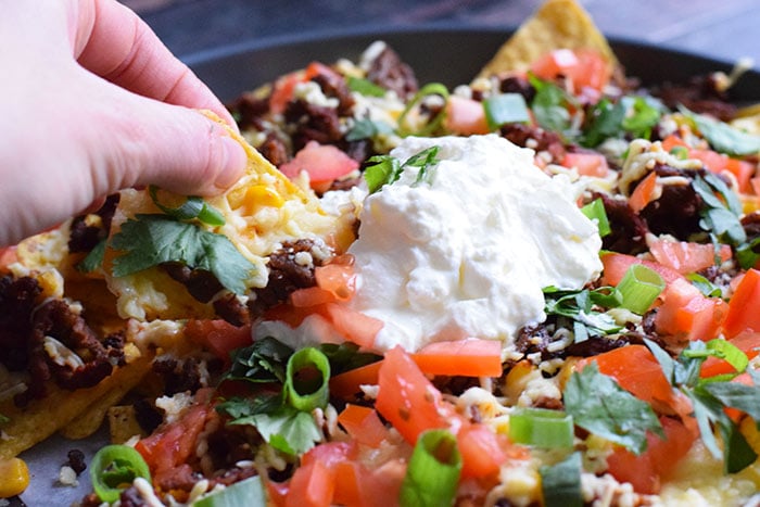 A hand taking a nacho from a plate of low FODMAP nachos