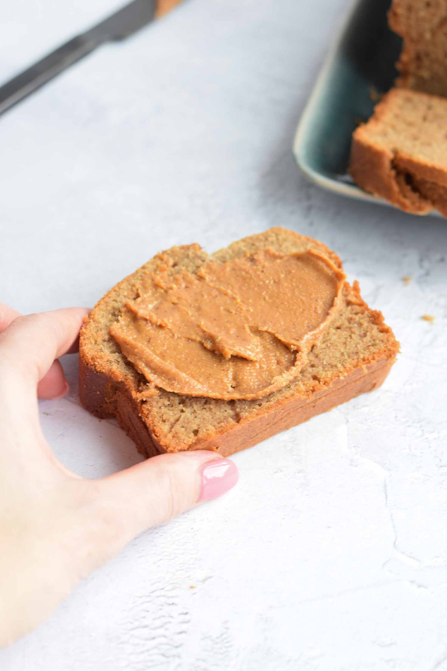 A hand holding a slice of banana bread with peanut butter