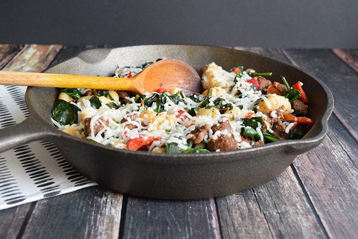 A skillet with gnocchi with sausage, spinach and grated goat cheese 