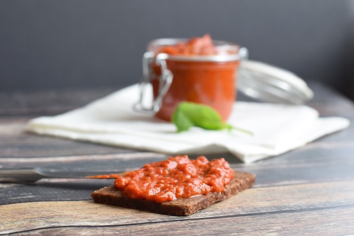 A roasted red pepper dip on a bread with a jar full of it behind