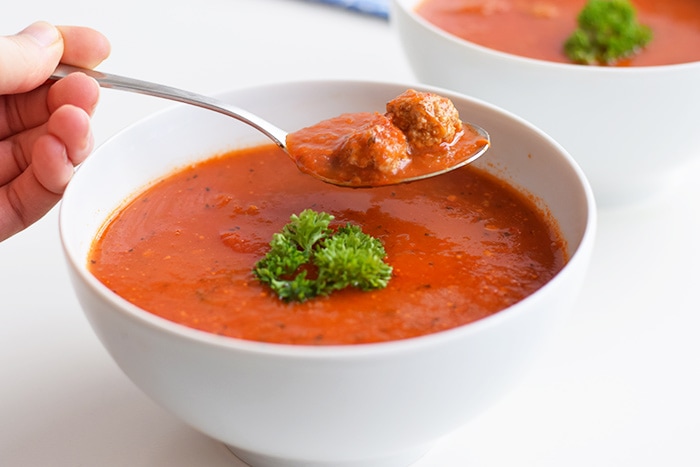 A spoon taking some low FODMAP tomato soup with meat balls from a bowl of soup
