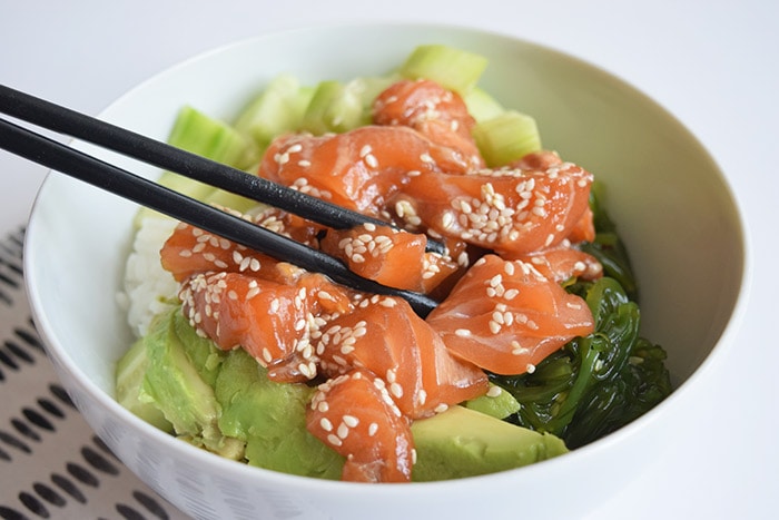 A low FODMAP poke bowl with salmon, somebody picking up a piece of salmon with chopsticks