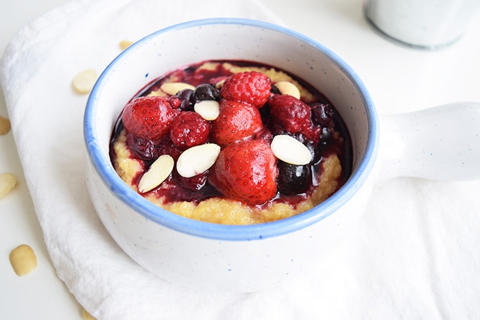 A bowl with low FODMAP polenta porridge topped with red fruits and almonds
