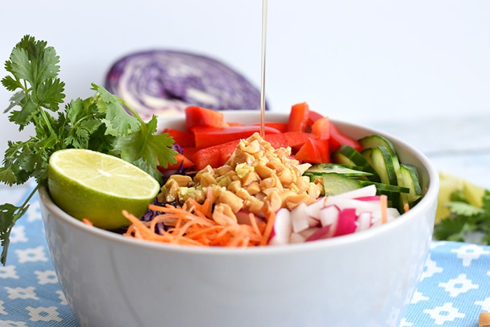 A low FODMAP Asian salad in a bowl where dressing is being poured on top