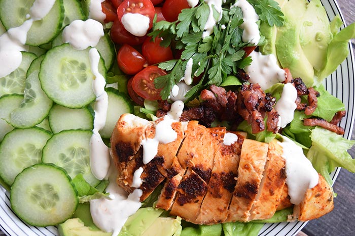 A grilled chicken salad with tomatoes, cucumber, bacon and avocado photographed from above