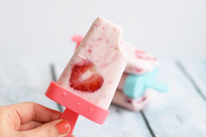 A hand holding a low FODMAP strawberry yoghurt popsicle with a few more popsicles in the background