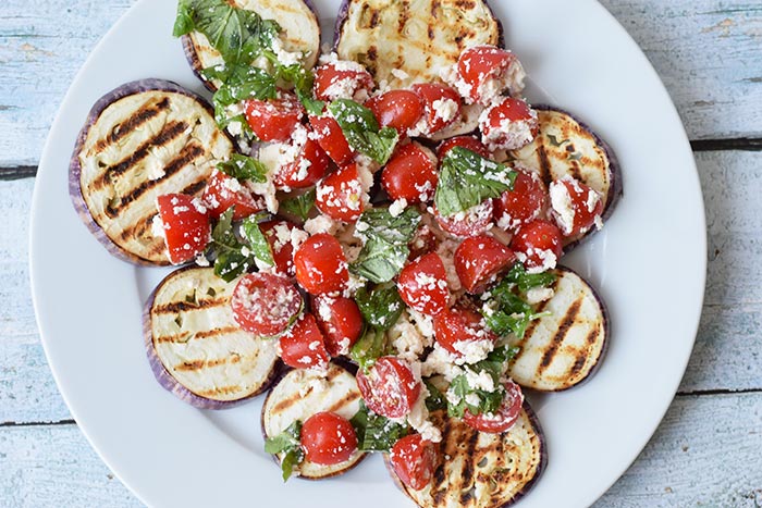 A plate with grilled eggplant with tomatoes and feta on top