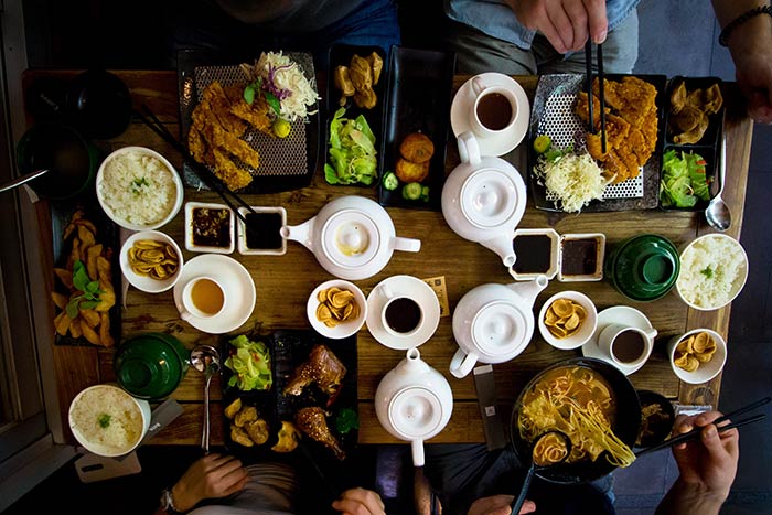 Een tafel met Aziatisch eten en vier personen die aan het eten zijn