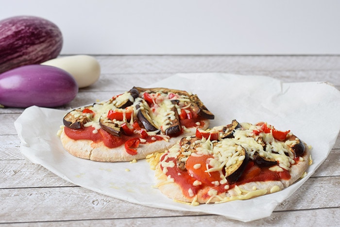 Twee low FODMAP pita pizza's met gegrilde groenten met drie aubergine's op de achtergrond