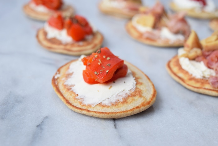 Low FODMAP blinis photographed from the side, with cream cheese and red bell pepper and with cream cheese, mushrooms and ham