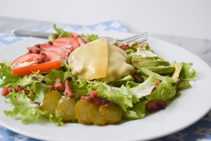 A salad with a burger, melted cheese, tomatoes, pickles and bacon