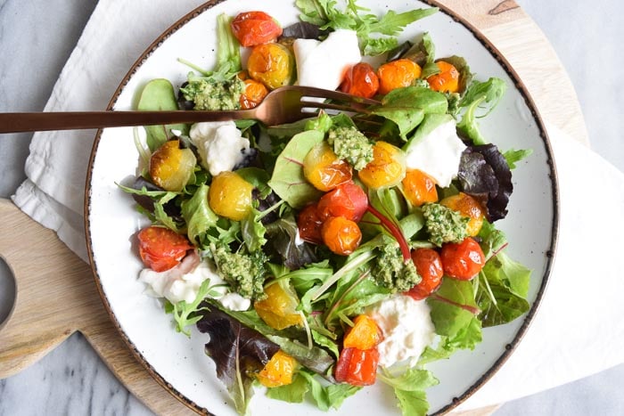 A plate of low FODMAP burrata salad with roasted tomatoes and pesto
