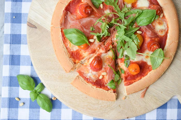 low FODMAP pizza parma ham with tomatoes on a wooden plate