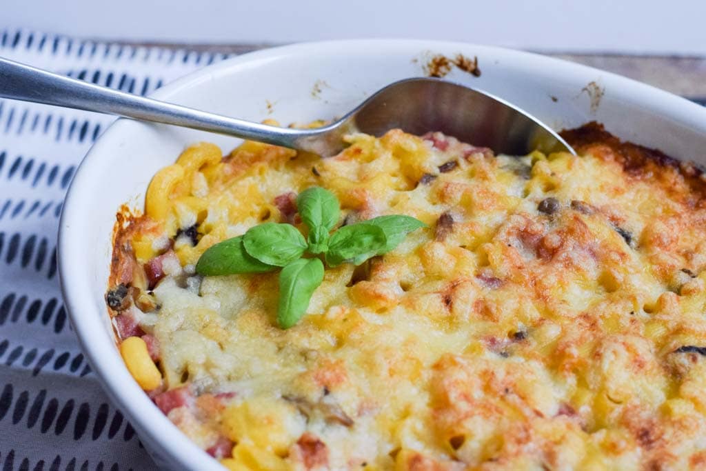 A mac and cheese casserole with fresh basil on top and a spoon in it