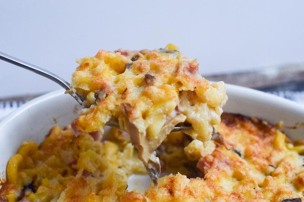 Somebody taking a spoonful out of a low FODMAP mac and cheese casserole with ham