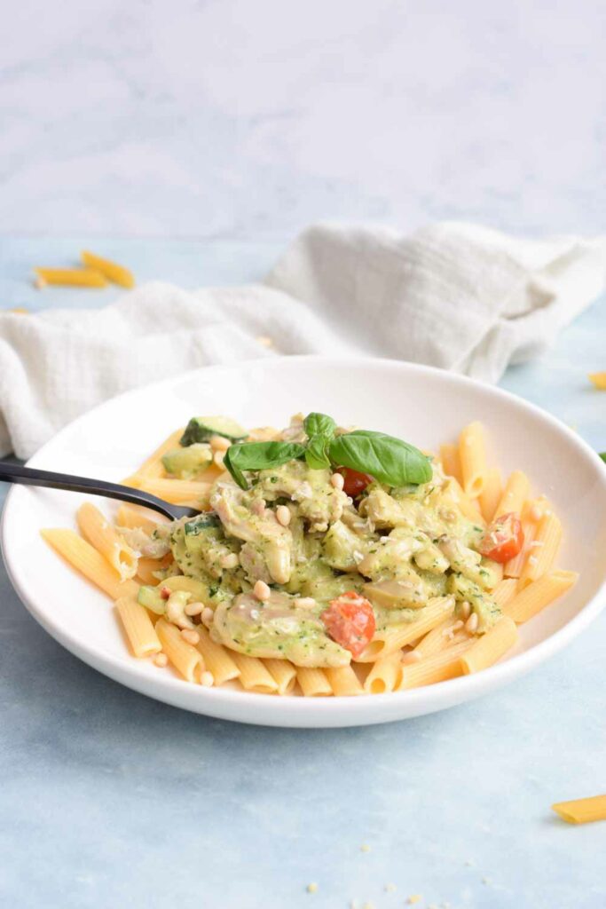 A plate with low FODMAP chicken pesto pasta with a spoon in it