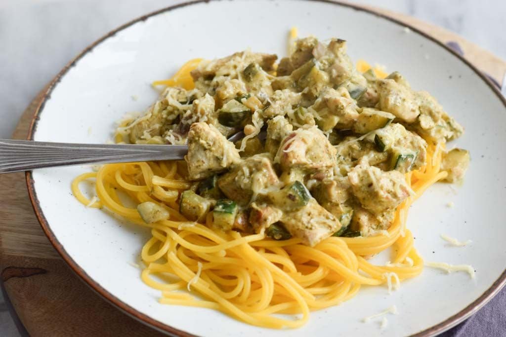 Pasta pesto with chicken on a plate with a fork in it