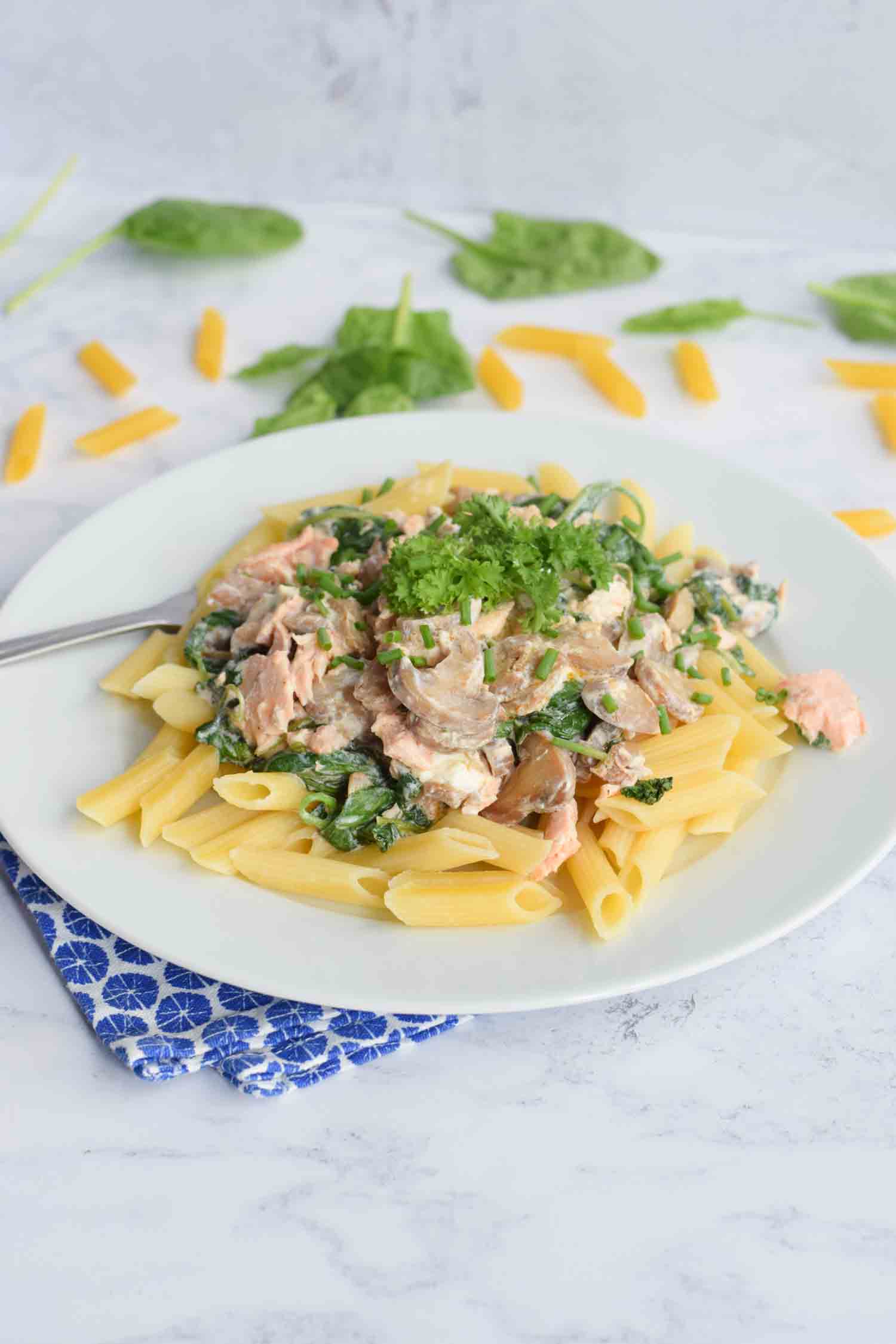 A plate with low FODMAP pasta with on top a creamy sauce with salmon, spinach and mushrooms