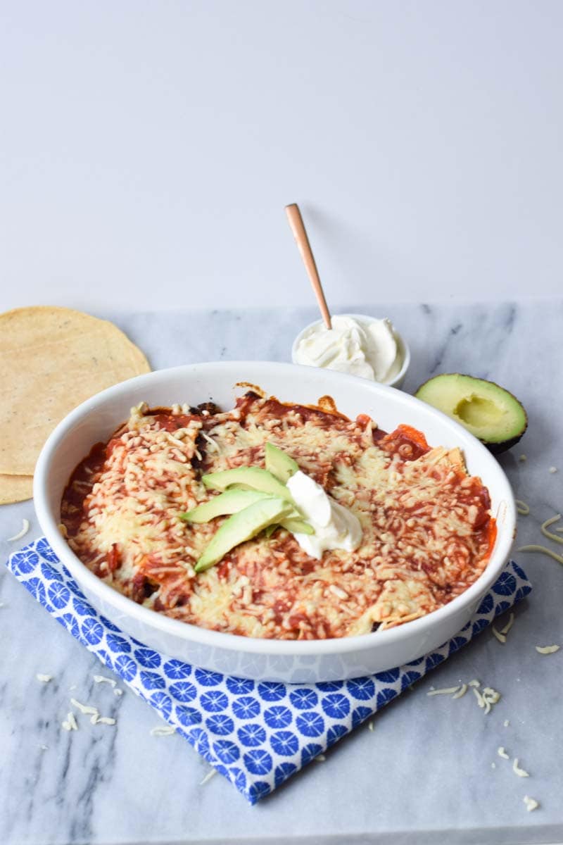 low fodmap enchiladas in a casserole with a blue napkin below and grated cheese around it