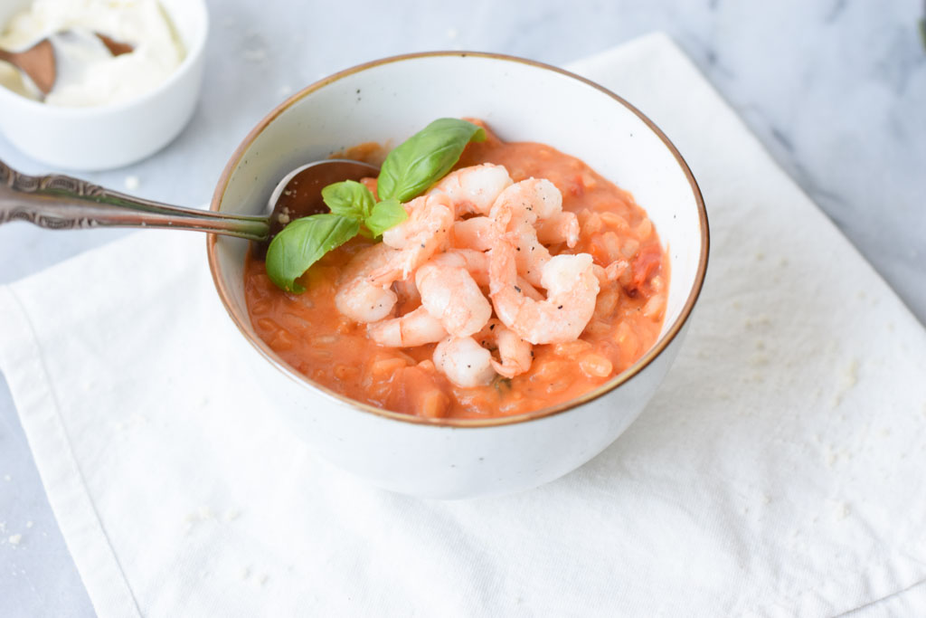 A bowl of tomato risotto with shrimps on a white napkin