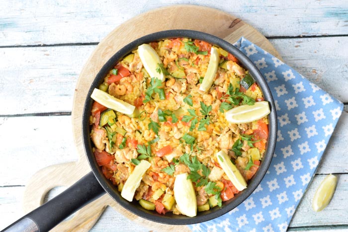 A pan of low FODMAP paella on a wooden plate with a light blue napkin next to it