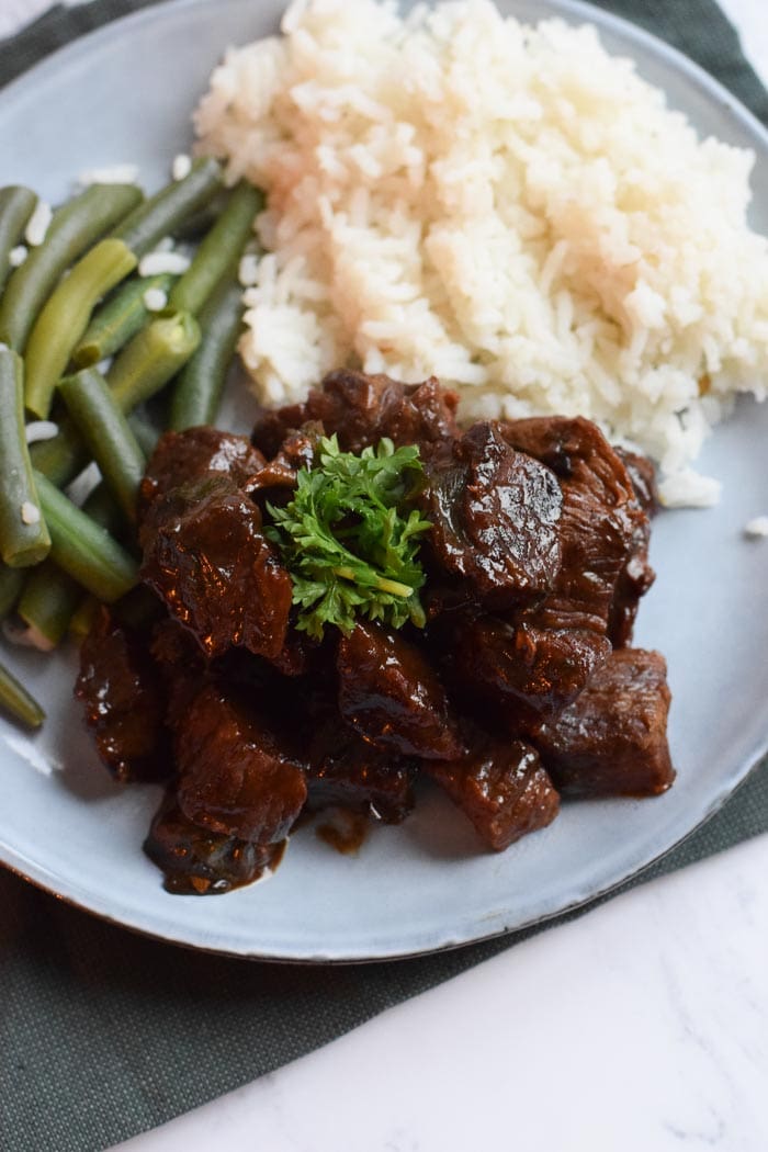 A plate with rice, green beans and beef stew, zoomed in on the beef stew with parsley on top