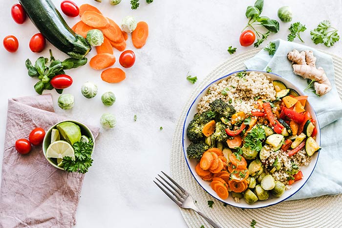 Een bord met couscous en veel groenten en naast het bord een heleboel losse groenten