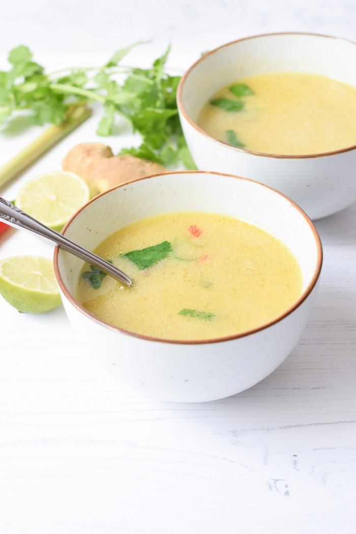 Two bowls of low FODMAP tom kha kai soup with lime, ginger and cilantro laying next to it