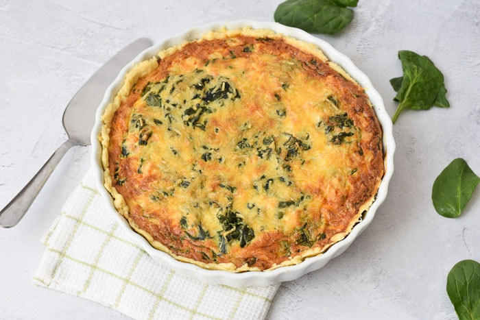 A salmon and spinach quiche with spinach leaves on the side