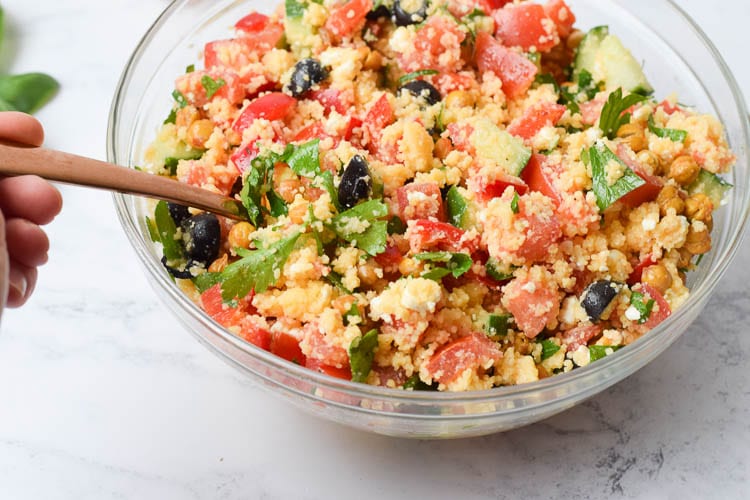 Gluten-free couscous salad in a glass bowl with a spoon in it