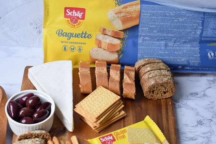 Een plank met Schär broodjes, kaas en olijven