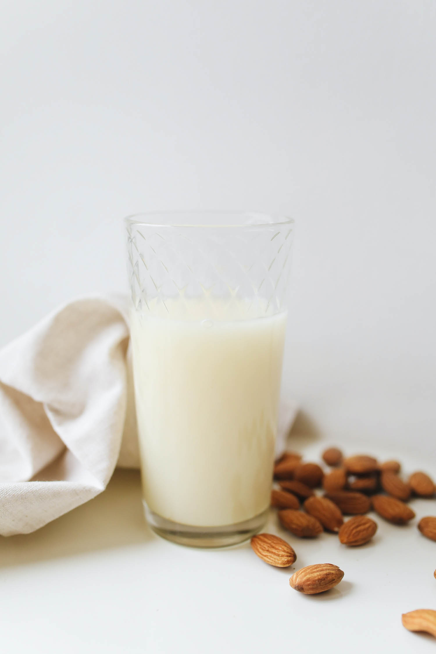 Homemade almond milk in a glass with almonds next to it