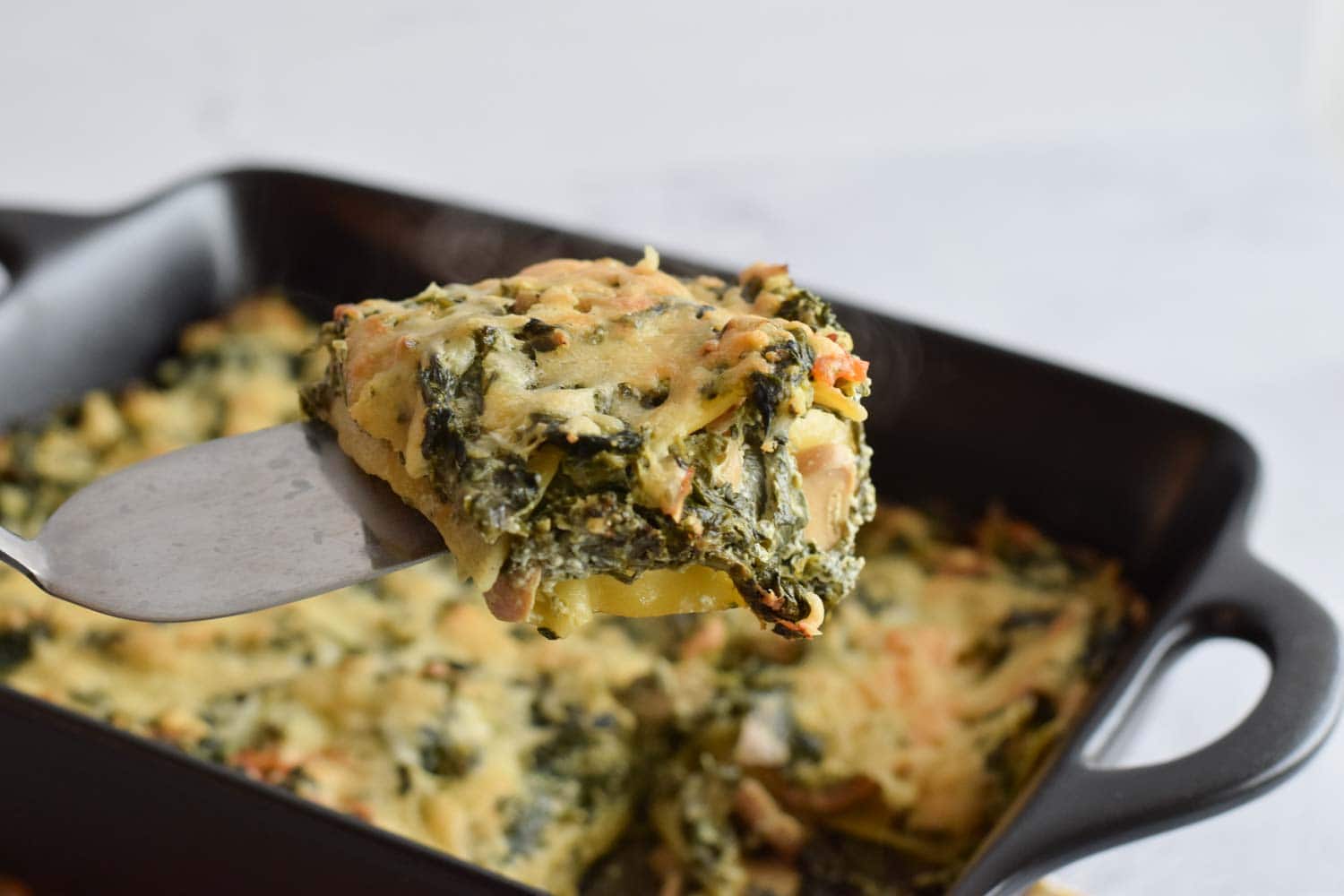 A spatula with a piece of low FODMAP salmon and spinach lasagna