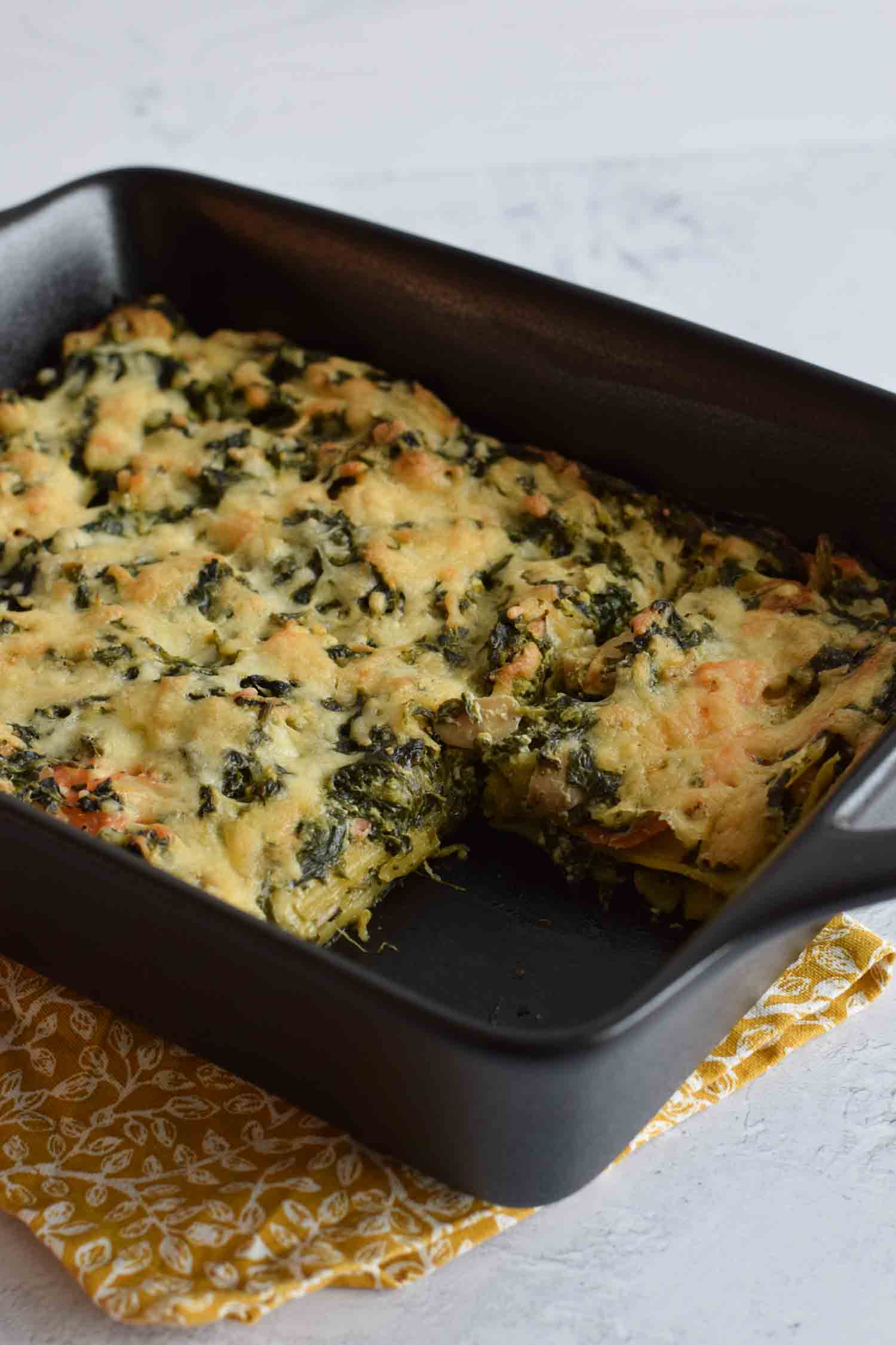 An oven dish with low FODMAP salmon and spinach lasagna with a piece out of it