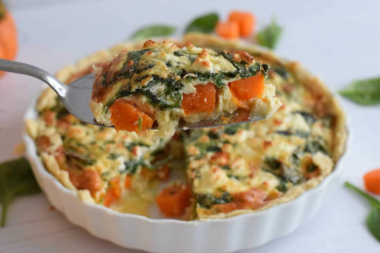 Low FODMAP pumpkin quiche with spinach and feta with one piece out of it